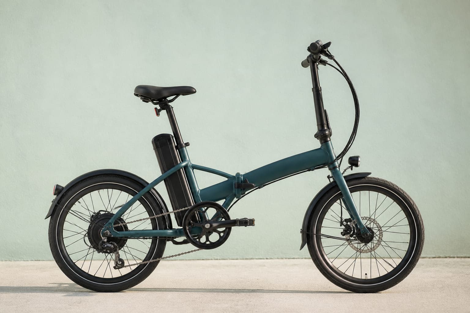 Falt-E-Bike in Petrol mit Hinterradmotor, abnehmbarem Akku hinter der Sattelstütze und Rahmenscharnier, von der Seite
